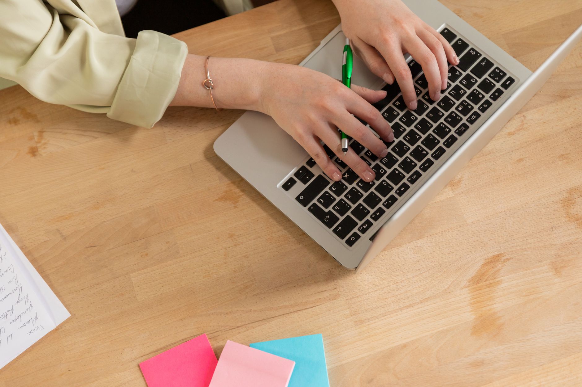 Hands typing on a laptop with a green pen and colorful sticky notes on a wooden desk — illustrating: Tampa IT Solutions vs National Providers: Which Fits Your Central Florida SMB Budget?